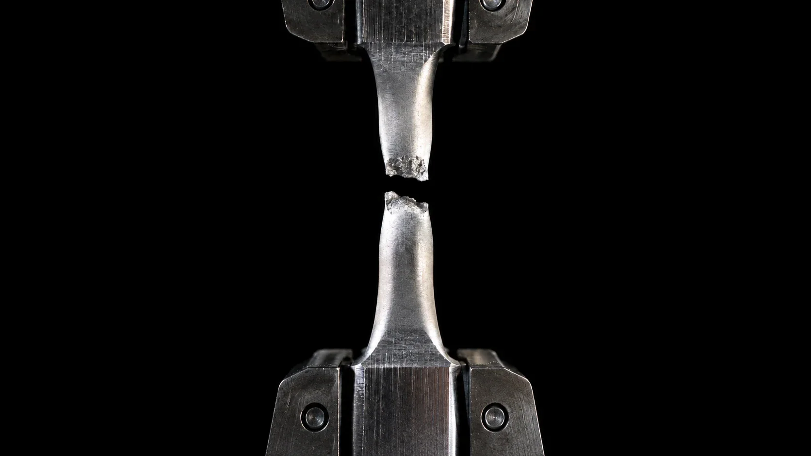 Metal tensile specimen broken in the grips of a testing machine, necked down to a rough, ductile fracture