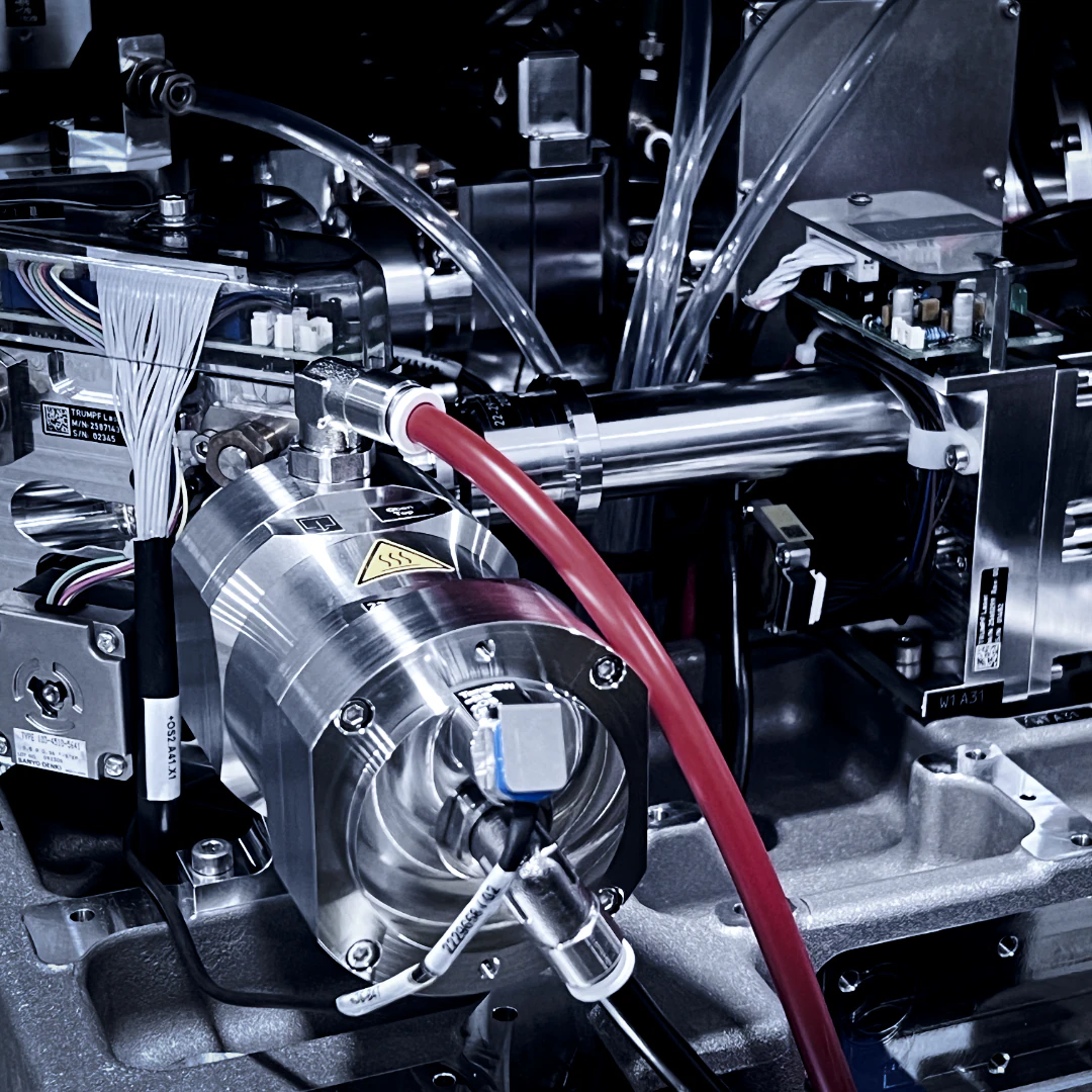 Close-up of a fiber laser cutting head and beam-delivery optics, with the red fiber-optic feed cable